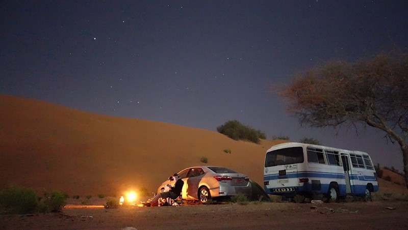 Alena Sirotná a Milan Rutkovský k snímku z Ománu napsali: Fotka je pořízena u paty duny pouště Wahiba Sands:22.5169475N, 58.6630197E. Abychom se vyhnuli turistické trase, kde se lítá ve velkých offroadech po dunách, píchli jsme prstem do místa bez názvu, kam vedla "cesta". V Ománu je kempování oblíbené a není problém si stan postavit téměř kde se vám zachce. Toto místo nám díky opuštěnému školnímu autobusu připomnělo film Into the wild (jen okolí bylo spíš reverzní). Lidé v Ománu a na venkově speciálně jsou neuvěřitelně pohostinní a chtějí, aby se cizinec u nich cítil nejlépe, jak to jen jde. Díky campingu v tomto místě se nám podařilo dostat na čaj a khubz k nedalekým beduínům a také na tréning mladých závodních velbloudů. Přátelství s několika Ománci trvá dodnes